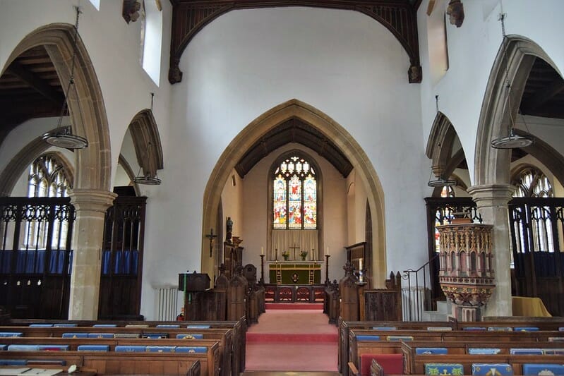 The inside of the Church with stained glass windows, pews and a tall archway
